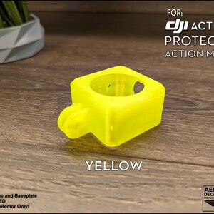 May include: A bright yellow 3D printed protector for a DJI Action 2 camera. The protector is designed to mount to the camera and protect it from damage. The text "FOR: DJI ACTION 2 PROTECTOR ACTION MOUNT YELLOW" is visible in the image.
