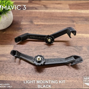 K&ouml;nnte beinhalten: Zwei schwarze Lichtmontages&auml;tze f&uuml;r DJI Mavic 3 Drohnen. Die S&auml;tze sind 3D-gedruckt und verf&uuml;gen &uuml;ber einen zentralen Einstellknopf und Befestigungspunkte. Der Text "LIGHT MOUNTING KIT BLACK" ist sichtbar.