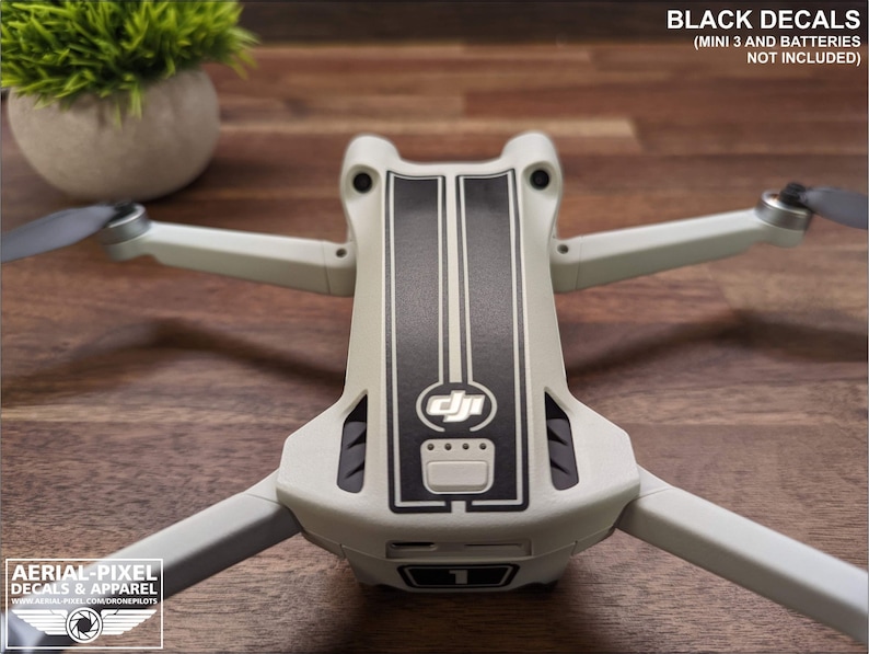 K&ouml;nnte beinhalten: Eine wei&szlig;e Drohne mit schwarzen Rennstreifen-Aufklebern auf der Oberseite. Die Drohne hat ein DJI-Logo auf der Vorderseite. Der Text "BLACK DECALS (MINI 3 AND BATTERIES NOT INCLUDED)" befindet sich oben im Bild.