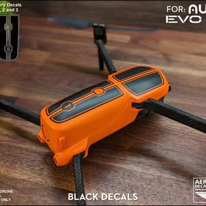 Pu&ograve; includere: Adesivi in ​​vinile nero per un drone Autel EVO Lite+ arancione. Gli adesivi sono numerati 1, 2 e 3. Il drone &egrave; su una superficie di legno.