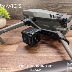K&ouml;nnte beinhalten: Schwarzes Lichtmontage-Kit f&uuml;r eine DJI Mavic 3 Drohne. Das Kit enth&auml;lt eine 3D-gedruckte Halterung und ist f&uuml;r die Aufnahme von Lichtern konzipiert. Die Drohne ist grau mit schwarzen Propellern. Der Text "LIGHT MOUNTING KIT BLACK" ist sichtbar.