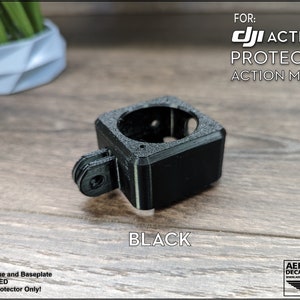 May include: Black 3D printed protector for a DJI Action 2 camera. The protector has a mount for attaching to a tripod or other accessories. "FOR: DJI ACTION 2 PROTECTOR ACTION MOUNT" is printed on the image.