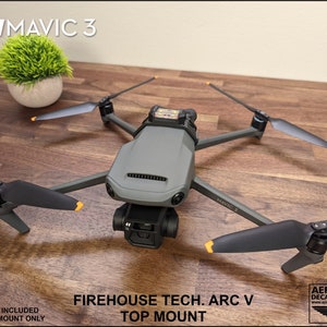 K&ouml;nnte beinhalten: Eine schwarz-graue Drohne mit orangefarbenen Akzenten, beschriftet mit "MAVIC 3", ist auf einem 3D-gedruckten Oberteil montiert. Die Halterung ist mit "FIREHOUSE TECH. ARC V TOP MOUNT" beschriftet.