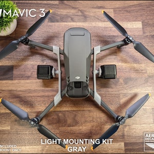 K&ouml;nnte beinhalten: Eine graue DJI Mavic 3 Drohne mit schwarzen Propellern und einem Lichtmontagesatz. Die Propeller haben gelbe Spitzen. Der Text "LIGHT MOUNTING KIT GRAY" ist sichtbar. Das Bild enth&auml;lt auch den Text "DJI MAVIC 3".