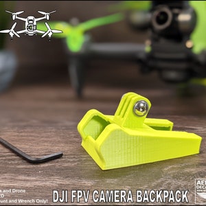May include: A bright green 3D printed camera mount for a DJI FPV drone. The mount is designed to hold a GoPro camera. The text "DJI FPV CAMERA BACKPACK" is printed on the image.