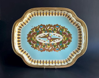 May include: Vintage metal serving tray with a light blue interior and a gold-colored rim. The tray features a central oval design with brown, green, yellow, and red leaf-like shapes. The rim has a repeating pattern of small leaf shapes.