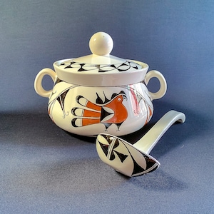 May include: A white ceramic soup tureen with a lid and matching ladle. The tureen features a hand-painted design of a bird in orange, black, and white. The lid and ladle are also decorated with black and white geometric patterns.