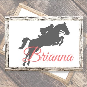May include: A white sign with a silhouette of a person riding a horse jumping over a fence. The name Brianna is written in pink cursive below the image.