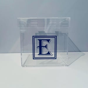 May include: A clear acrylic box with a lid. The box has a blue letter "E" in a decorative frame on the front.