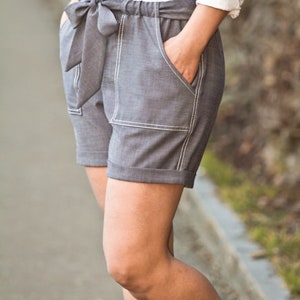 May include: Gray linen shorts with a white top stitch detail and a large bow at the waist.