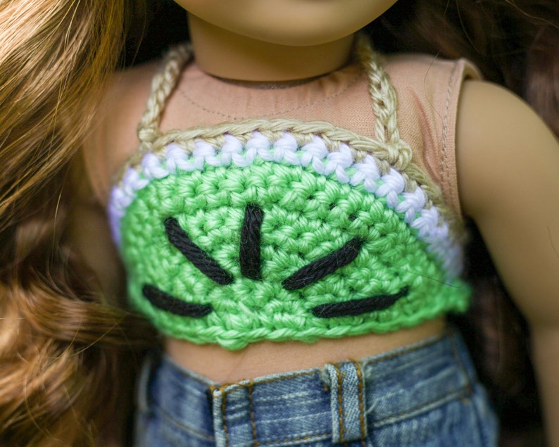 May include: A green crocheted halter top with black stitching, resembling a watermelon. The top is worn by a doll with brown hair and a tan shirt.