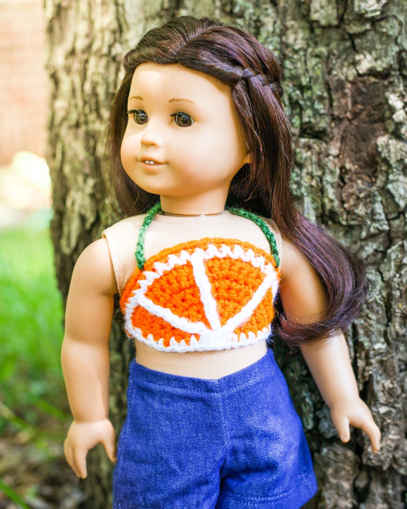 May include: A doll wearing a crocheted orange and white top with a blue denim skirt.