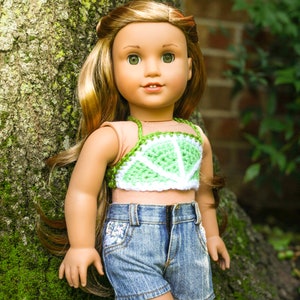 May include: A doll with long brown hair wearing a green and white crocheted lime slice top and blue denim shorts.