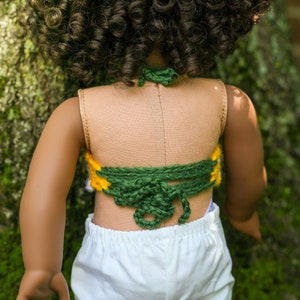 May include: A doll wearing a green and yellow crocheted halter top with a white skirt.