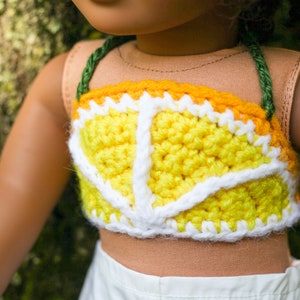 May include: A yellow and white crocheted top with a green strap. The top is shaped like a lemon slice.
