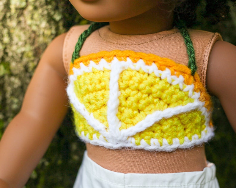 May include: A yellow and white crocheted top with a green strap. The top is shaped like a lemon slice.