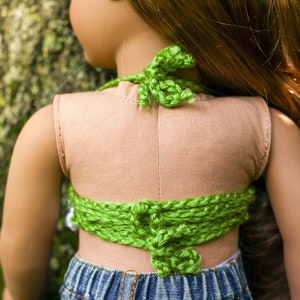 May include: A green crocheted halter top with a tied back. The top is worn over a light brown tank top and blue denim shorts.