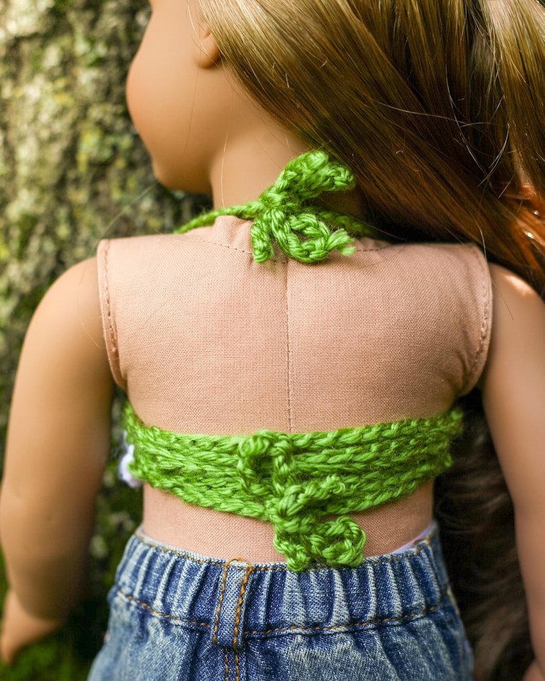 May include: A green crocheted halter top with a tied back. The top is worn over a light brown tank top and blue denim shorts.