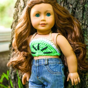 May include: A doll with long, wavy, auburn hair wearing a green and white crocheted halter top and blue denim shorts.
