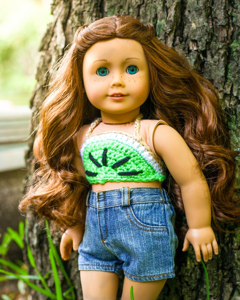 May include: A doll with long, wavy, auburn hair wearing a green and white crocheted halter top and blue denim shorts.