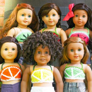 May include: Six dolls wearing different colored crocheted tops. The tops are all in a similar style, with a halter neck and a wide band across the chest. The dolls have different hair colors and styles, and they are all smiling.