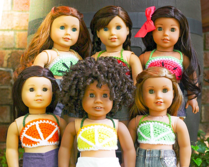 May include: Six dolls wearing different colored crocheted tops. The tops are all in a similar style, with a halter neck and a wide band across the chest. The dolls have different hair colors and styles, and they are all smiling.