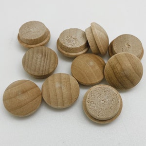 Peut inclure: Un groupe de dix boutons ronds en bois, tous de même taille et de même forme. Les boutons sont de couleur brun clair et ont une surface lisse légèrement texturée.