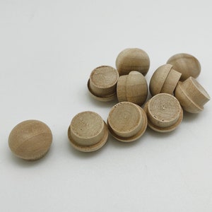 May include: A group of 10 small, round, wooden knobs in a natural wood color. The knobs are about 1 inch in diameter and have a smooth, rounded surface.