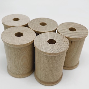 May include: Six wooden spools, all the same size and shape, are stacked on a white surface. The spools are a light brown color and have a smooth, unfinished surface.