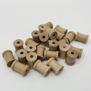 May include: A collection of small, unfinished wooden spools. Each spool has a cylindrical body with a central hole and flared ends. The spools are scattered on a white surface, suggesting a craft or DIY project.