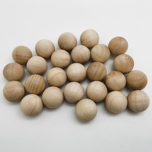May include: A group of 20 natural wood balls, arranged in a loose pile on a white background. The balls are all the same size and are a light brown colour.