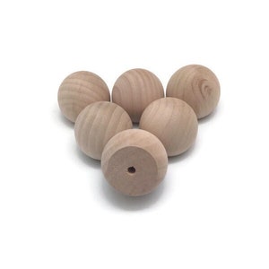 May include: Five unfinished wooden balls, each with a smooth surface. The balls are arranged in a triangular shape, with the bottom ball having a small hole in the center.