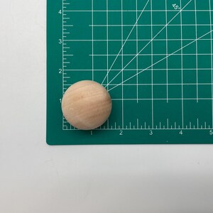 May include: A close-up of a natural wood sphere on a green cutting mat with white markings. The sphere is about 1 inch in diameter.