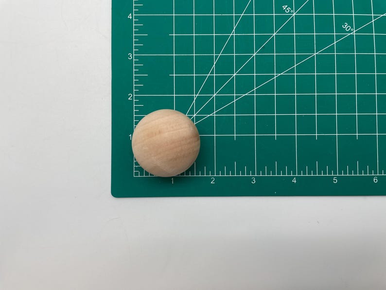 May include: A close-up of a natural wood sphere on a green cutting mat with white markings. The sphere is about 1 inch in diameter.