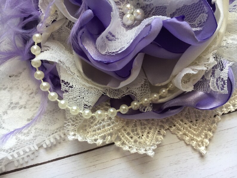 May include: A purple and white flower made of fabric with a pearl and lace trim.