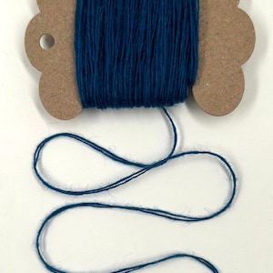 May include: A spool of teal-colored yarn. The yarn is wound around a brown, die-cut cardboard spool. The yarn extends from the spool in a loose, wavy line. Ideal for crafting and textile projects.
