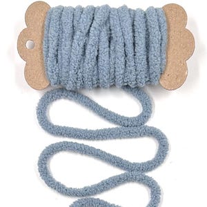 May include: A spool of soft, blue yarn. The yarn is thick and fluffy, with a textured appearance. The spool is made of cardboard and has a flower-like shape on each end. The yarn is unwound in a wavy pattern.