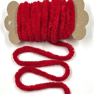 May include: A spool of vibrant red, plush yarn. The yarn is tightly wound around a cardboard spool with a decorative edge. A length of the yarn extends from the spool, showcasing its soft, textured appearance. Ideal for crafting projects.