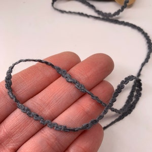 Puede incluir: Una cinta decorativa gris con borde festoneado. La cinta est&aacute; hecha de un material suave y tejido. La cinta se muestra sobre un fondo neutro. Adecuada para diversos proyectos de artesan&iacute;a y costura.