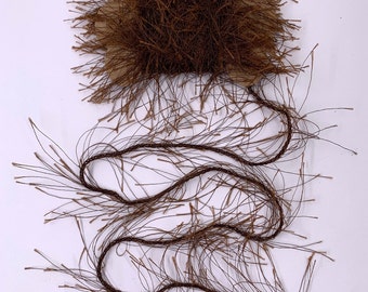 May include: A spool of brown decorative thread with a fuzzy texture. The thread is attached to a cardboard base and extends in a wavy pattern. The thread has small, thin, hair-like strands extending from it.