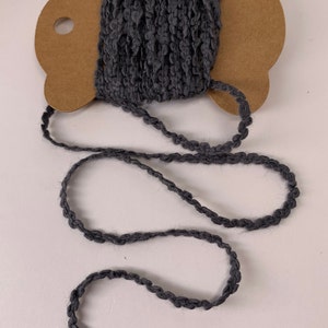 Puede incluir: Un carrete de hilo gris oscuro con un dise&ntilde;o texturizado y en bucle. El hilo est&aacute; desenrollado, revelando una longitud del mismo material. El carrete es de cart&oacute;n marr&oacute;n. Ideal para manualidades y proyectos textiles.