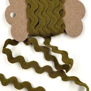Puede incluir: Cinta ondulada verde oliva en un carrete de cartón. La cinta está desenrollada, mostrando su diseño en zigzag texturizado. El carrete tiene una forma decorativa con un agujero para colgar. Ideal para manualidades y costura.
