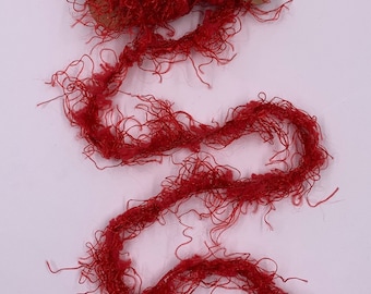 May include: A spool of vibrant red yarn with a fuzzy, textured appearance. The yarn is unwound, creating a flowing, wavy line. The spool is made of a brown, cardboard-like material. Ideal for crafting and textile projects.