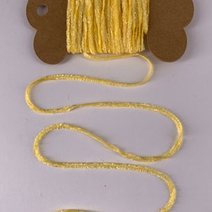 May include: A spool of bright yellow, textured yarn. The yarn is wound around a brown cardboard spool with a decorative edge. The yarn extends from the spool in a loose, wavy line, suggesting it's ready for crafting projects.