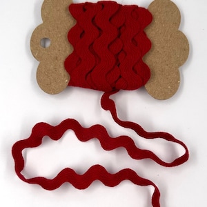 May include: A spool of red, wavy ribbon. The ribbon is wound around a cardboard spool with a decorative shape. The ribbon is a deep red color and has a textured, wavy edge. The ribbon is unwound from the spool.