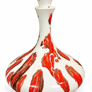 Può includere: Un decanter in ceramica con base ampia e arrotondata e collo sottile, sormontato da un tappo abbinato. La superficie è bianco sporco con finitura lucida, caratterizzata da audaci pennellate verticali in arancione vivace e marrone scuro.