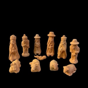 May include: A collection of twelve unglazed terracotta figurines depicting a nativity scene. The set includes standing figures in robes and hats, a small infant figure, and several animal figures, all featuring a natural light brown clay finish.