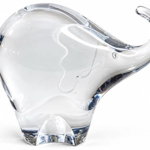 Könnte beinhalten: Eine klare Glasfigur in Form eines Elefanten. Die Skulptur weist eine glatte, transparente Oberfläche mit einem stilisierten, nach oben gebogenen Rüssel und einem abgerundeten Körper auf. Das Design ist schlicht und betont die Reflexion des Glases.