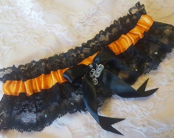 May include: Black lace garter with an orange satin ribbon and a silver charm. The charm has a motorcycle design and rhinestones.