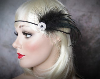 May include: A black feather headband with a sparkling rhinestone embellishment. The headband features a thin black band and is adorned with a cluster of black feathers. The accessory is a vintage-inspired piece, perfect for themed events or special occasions.